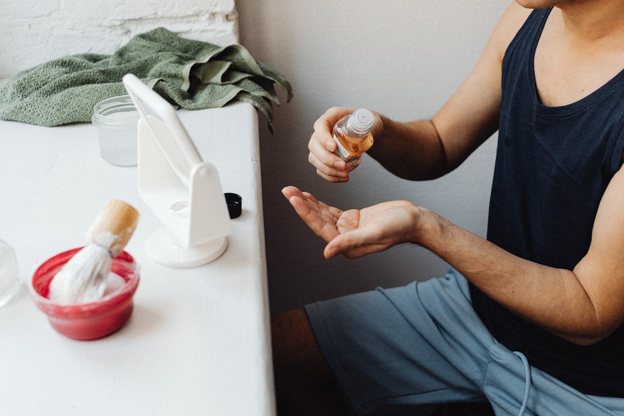Adult man applying aftershave in a casual bathroom setup with mirror and shaving accessories.
