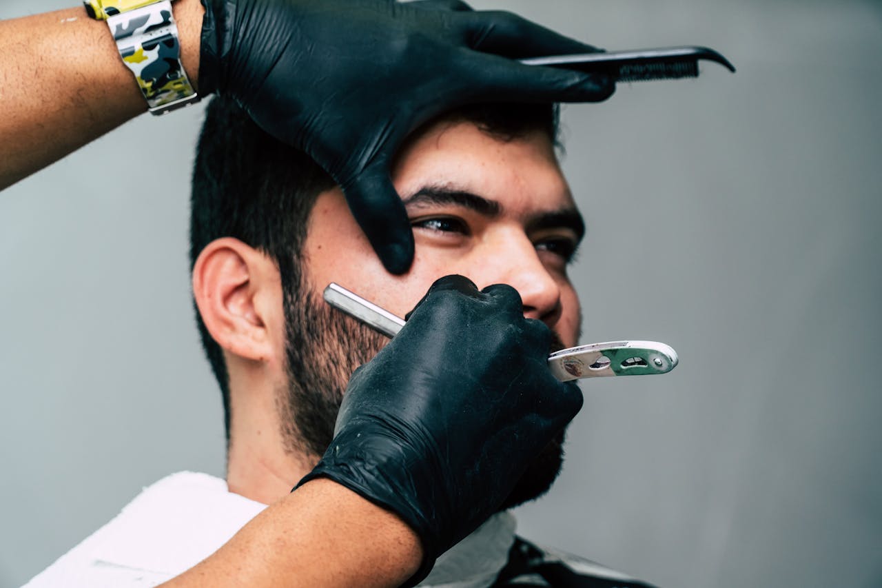 Close-up of a barber shaving a mans beard with precision in a contemporary barbershop setting.