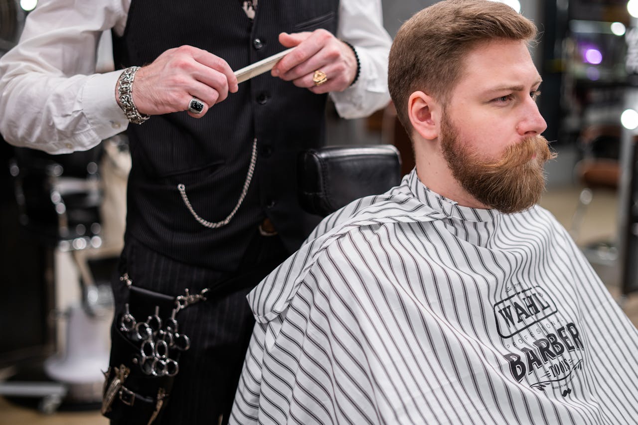 A barber meticulously grooming a bearded man in a stylish barbershop setting, showcasing modern mens grooming.