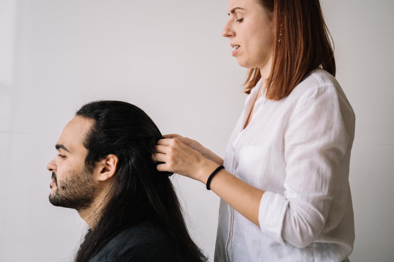 Professional hairdresser braiding a mans long hair, focusing on style and modern grooming.